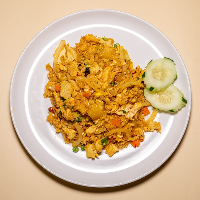 A plate of Racha Café's pineapple fried rice with chicken, vegetables, and cucumber slices.