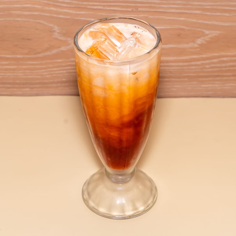 A tall glass of Racha Café's iced Thai tea with milk and ice cubes.