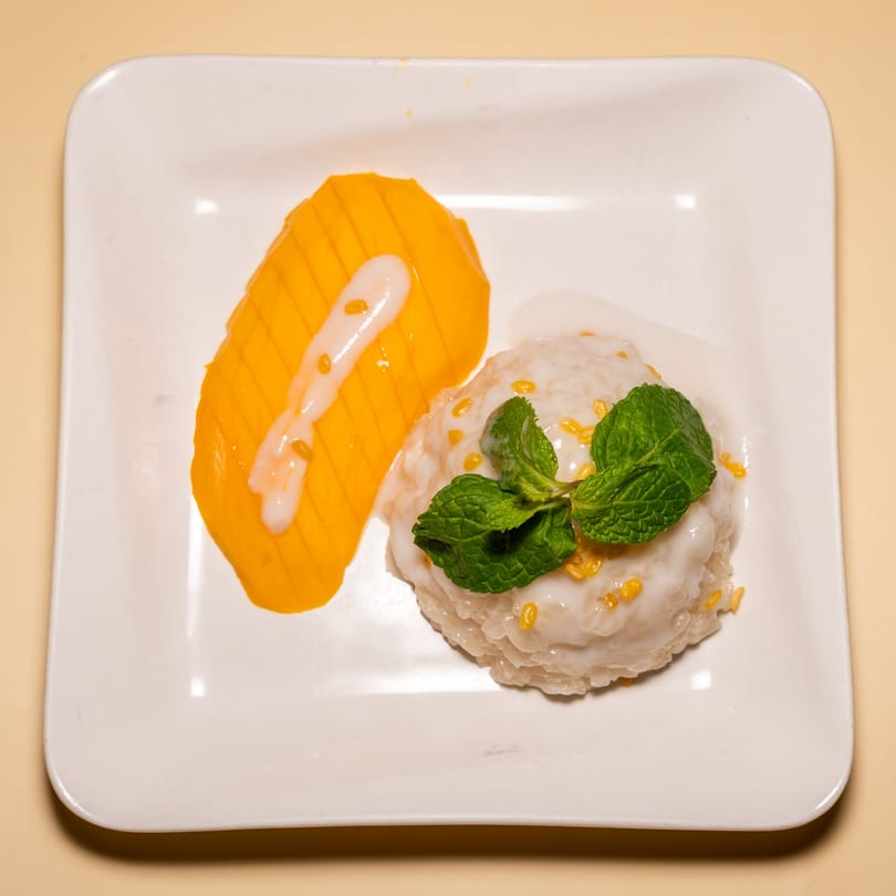 Mango sticky rice with coconut milk and mint on a white rectangular plate.