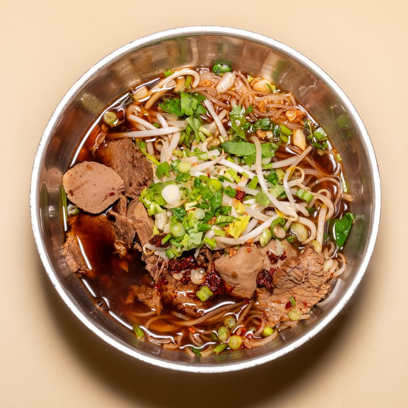 Racha Café's Thai boat noodles with beef, meatballs, bean sprouts, and green onions in a metal bowl.