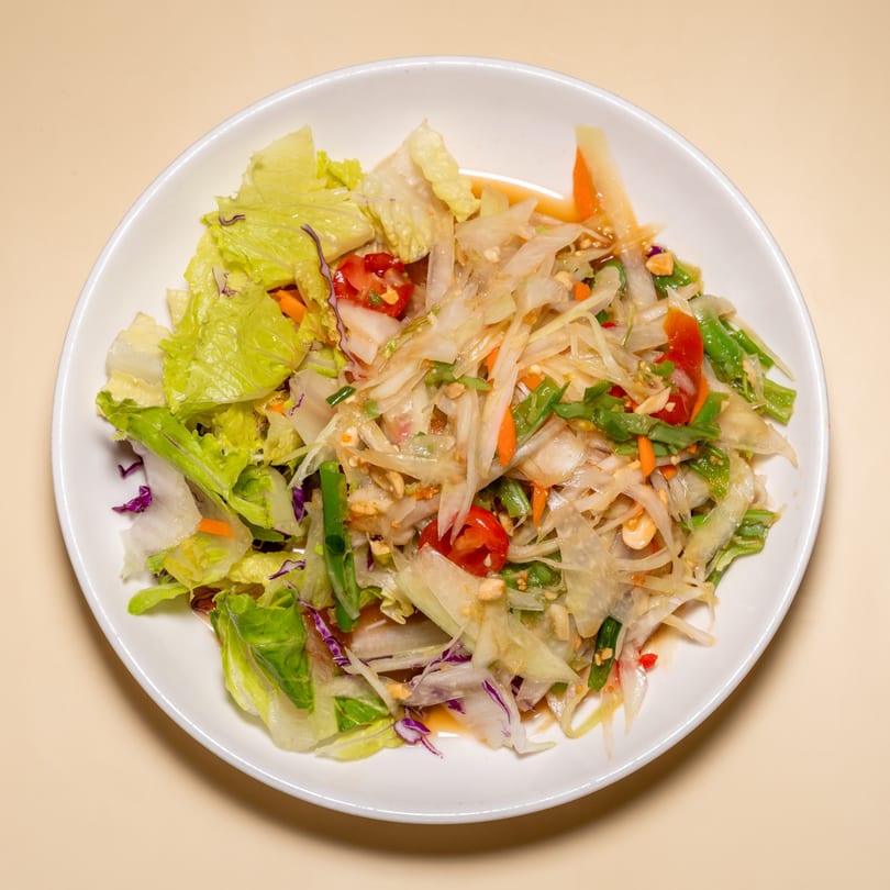 A white plate of Racha Café's Thai papaya salad with lettuce, tomatoes, and peanuts.