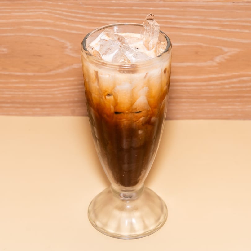 Iced Thai tea with a creamy top layer and ice in a tall glass.
